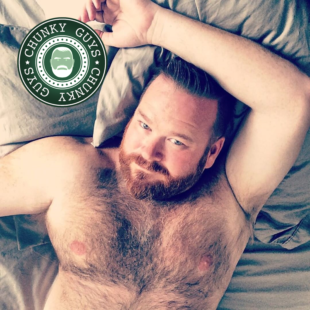 Man with hairy chest lying down on a bed, one arm above his head, looking up at the camera