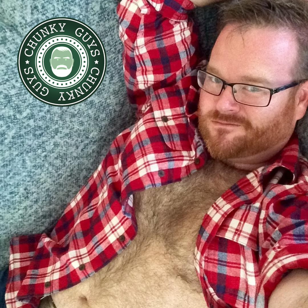 Ginger bearded guy wearing glasses and open red check shirt showing off his hairy chest