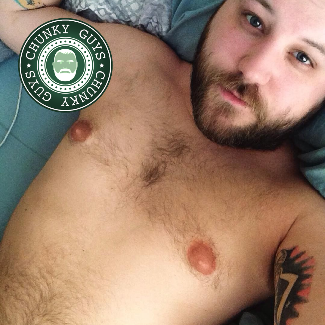 Bearded young guy with blue eyes and tattoos in bed looking up at the camera
