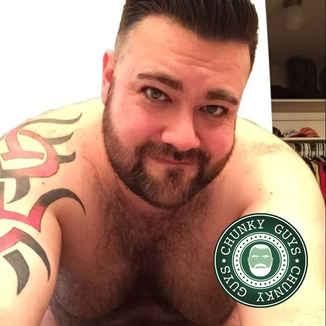 Chunky guy with hairy chest and beard looking at the camera with a grin