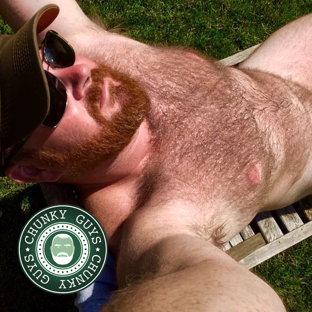 Bearded ginger beary guy with a hairy chest wearing sunglasses and a cap sunbathing