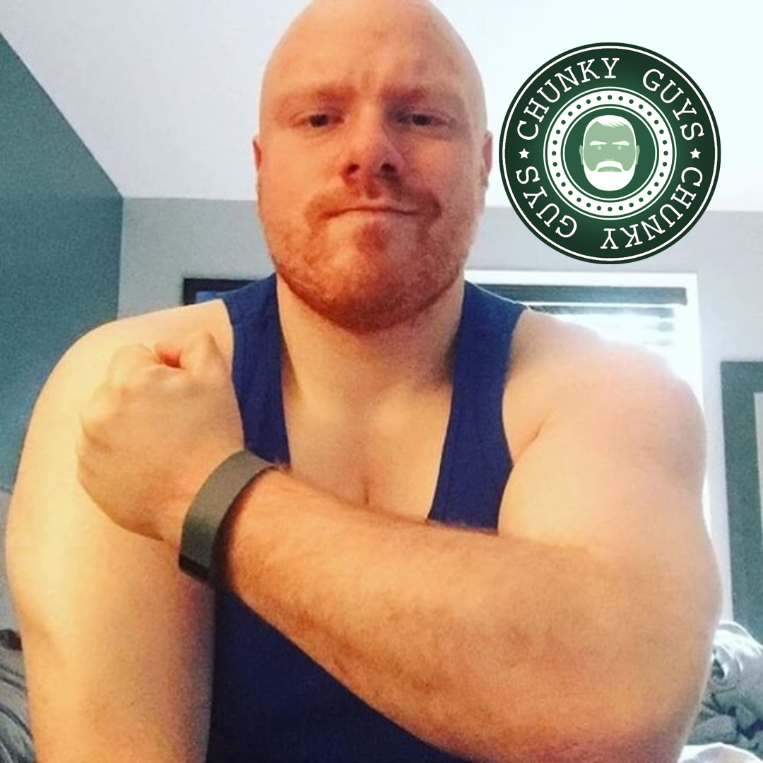 Ginger guy with stubble and a shaved head, wearing a blue vest and flexing his bicep