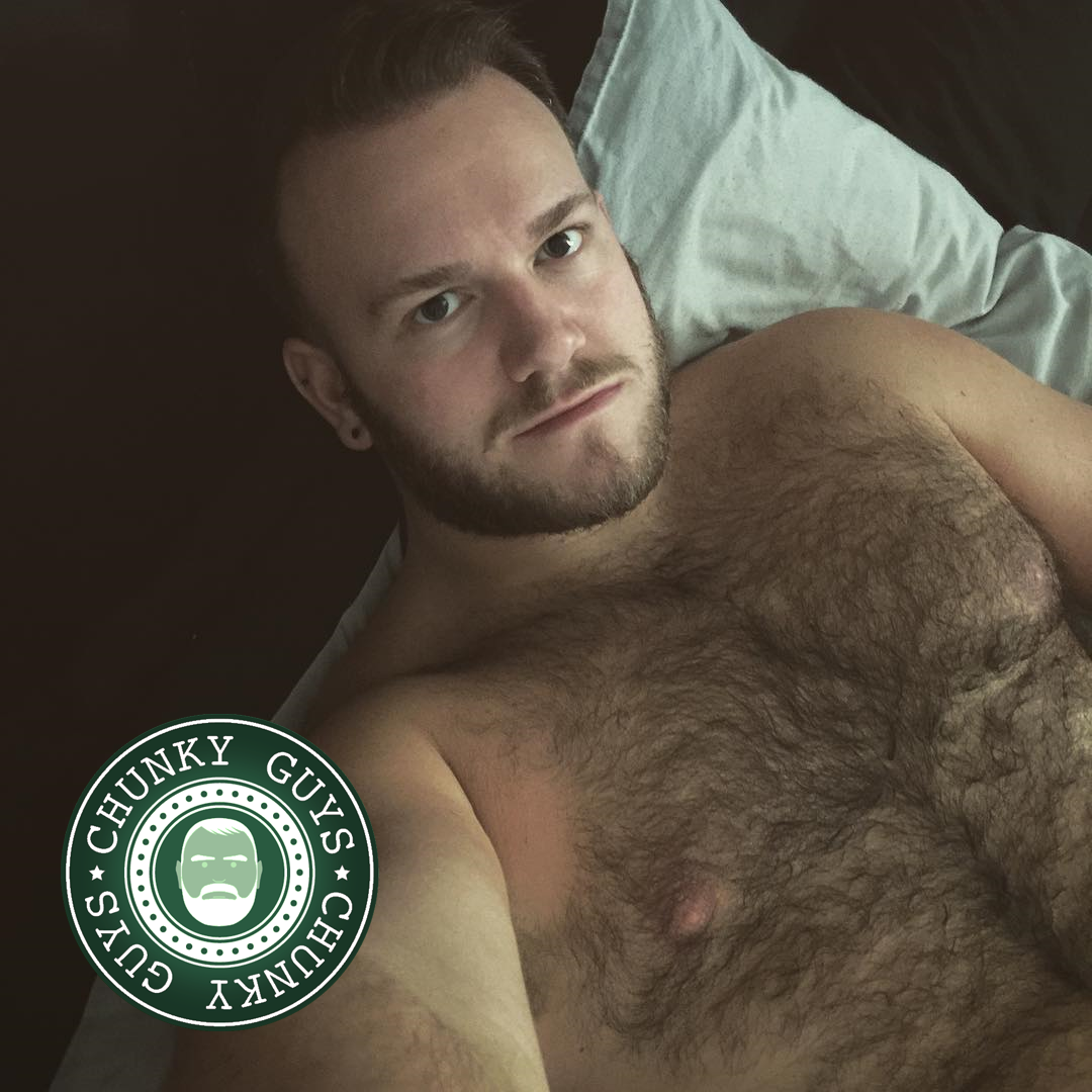 Hairy young cubby guy laying on a bed looing up at the camera