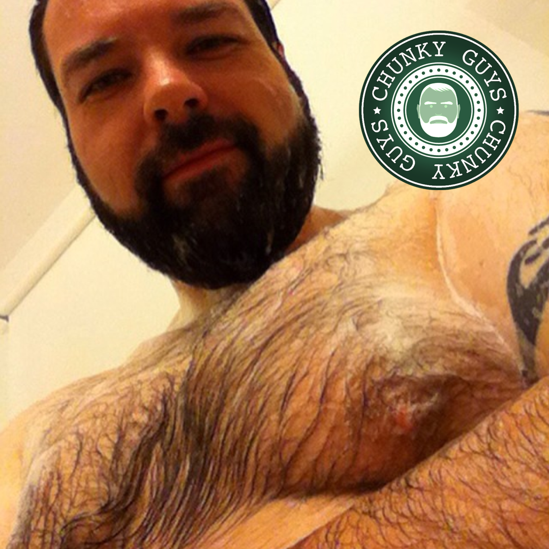 Bearded and hairy guy in the shower with soap over his chest looking down at the camera