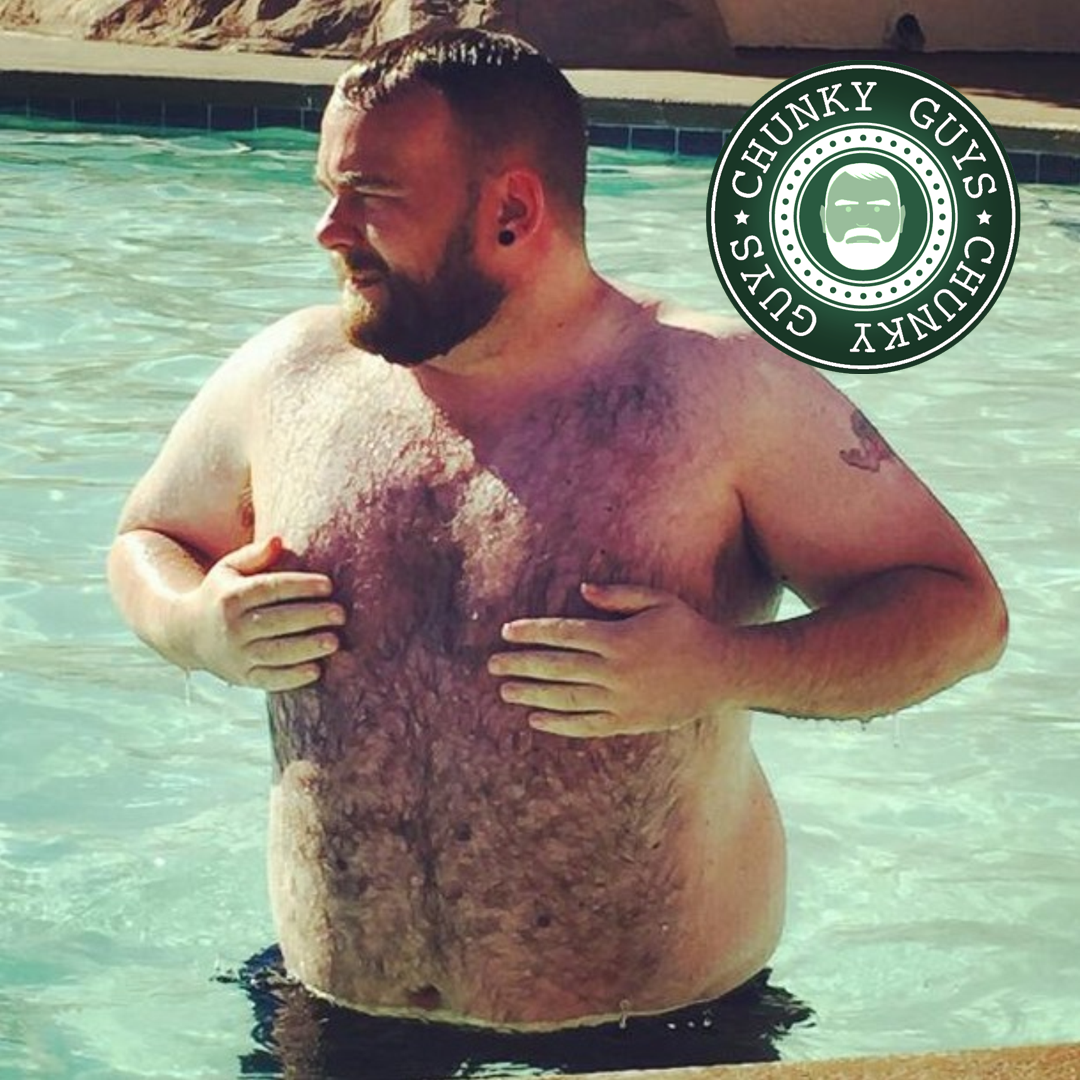 Hairy bearded chunky guy with tunnels in his ears standing in a pool with both hands over his chest