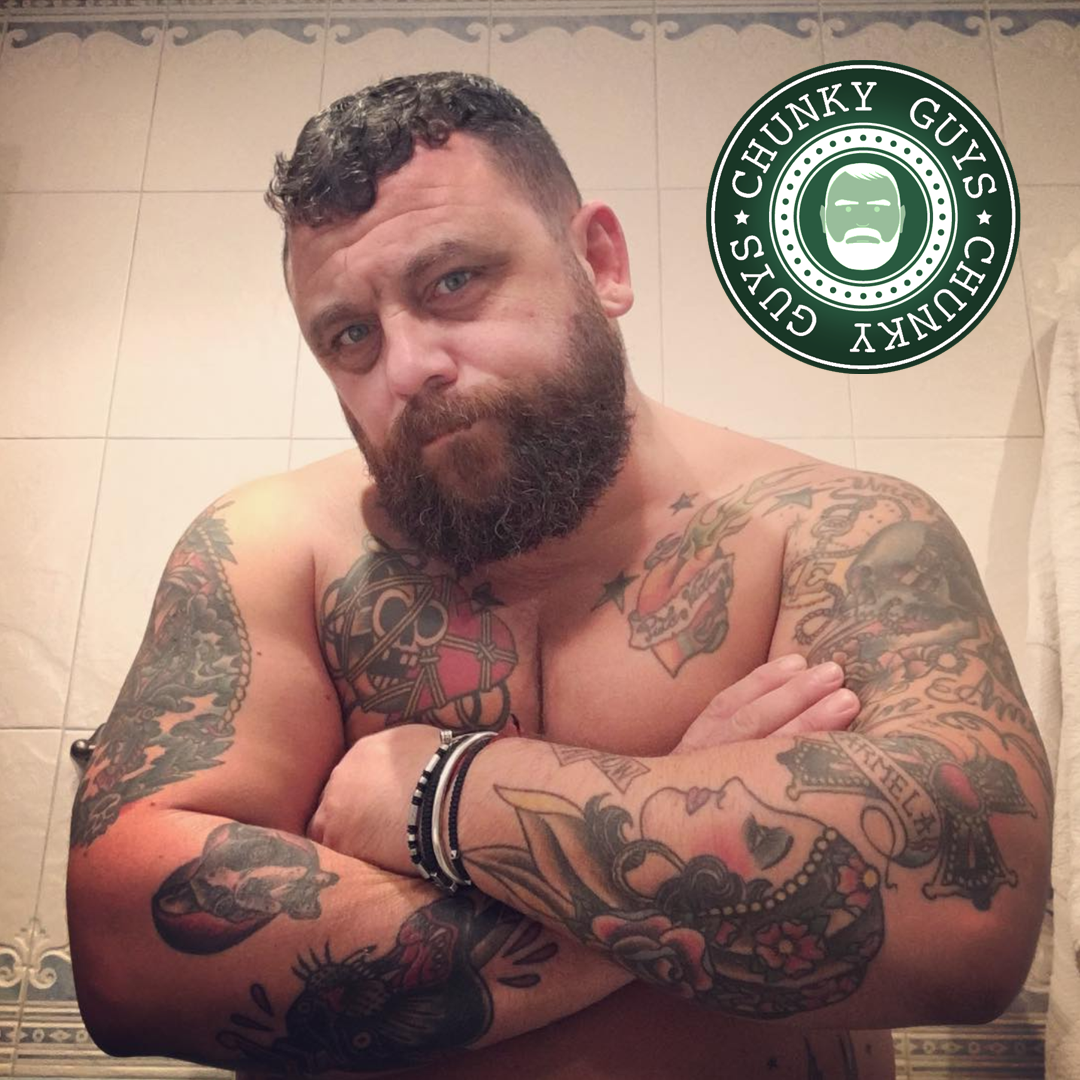 Tattooed bearded bear with curly hair folding his arms