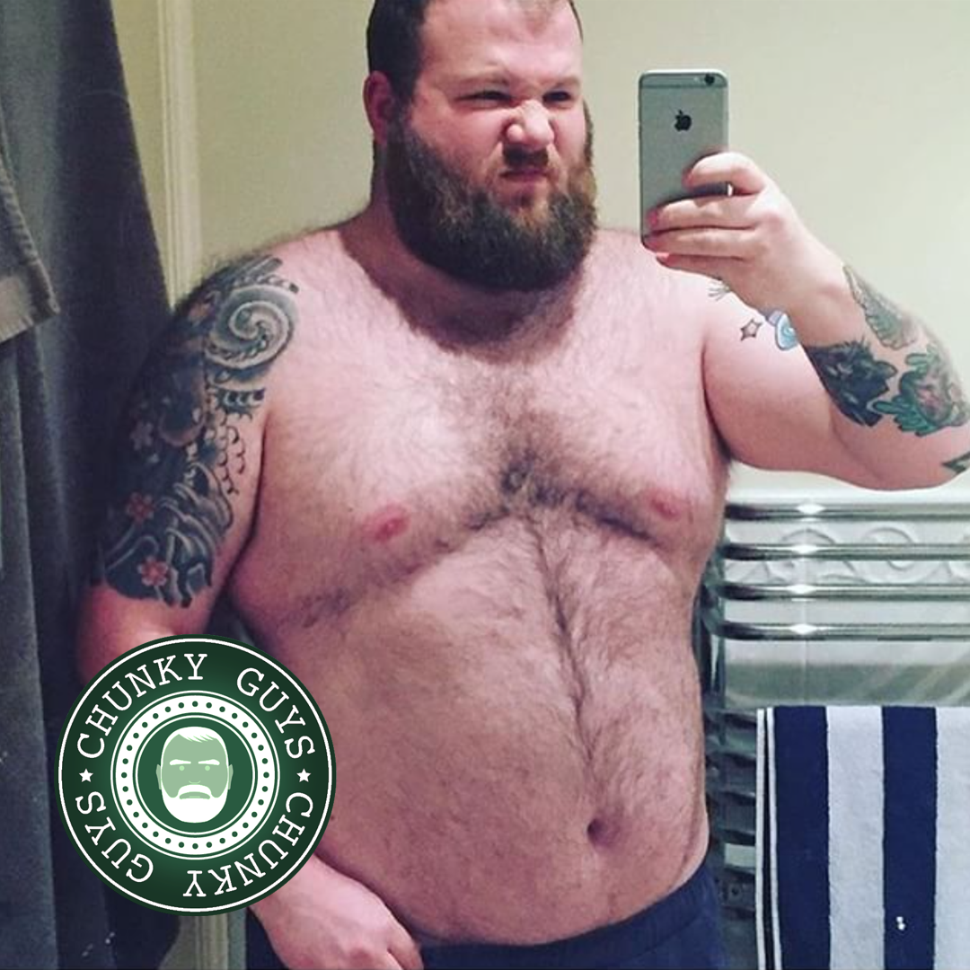 Hairy bearded tattooed chunky guy pulling a face in the mirror as he takes a photo of himself