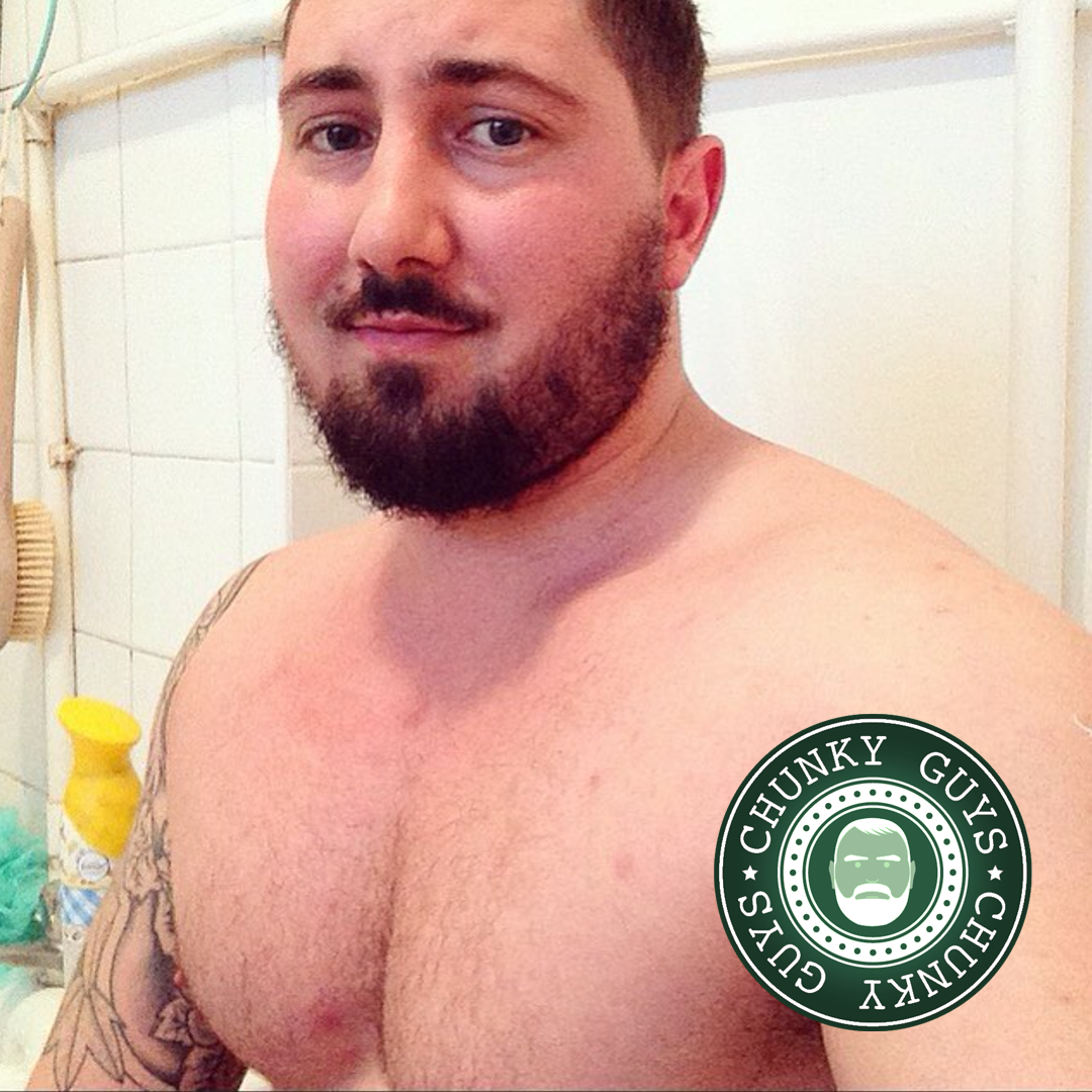Tattooed muscle cub with dark hair and a beard takes a photo of himself in the bathroom